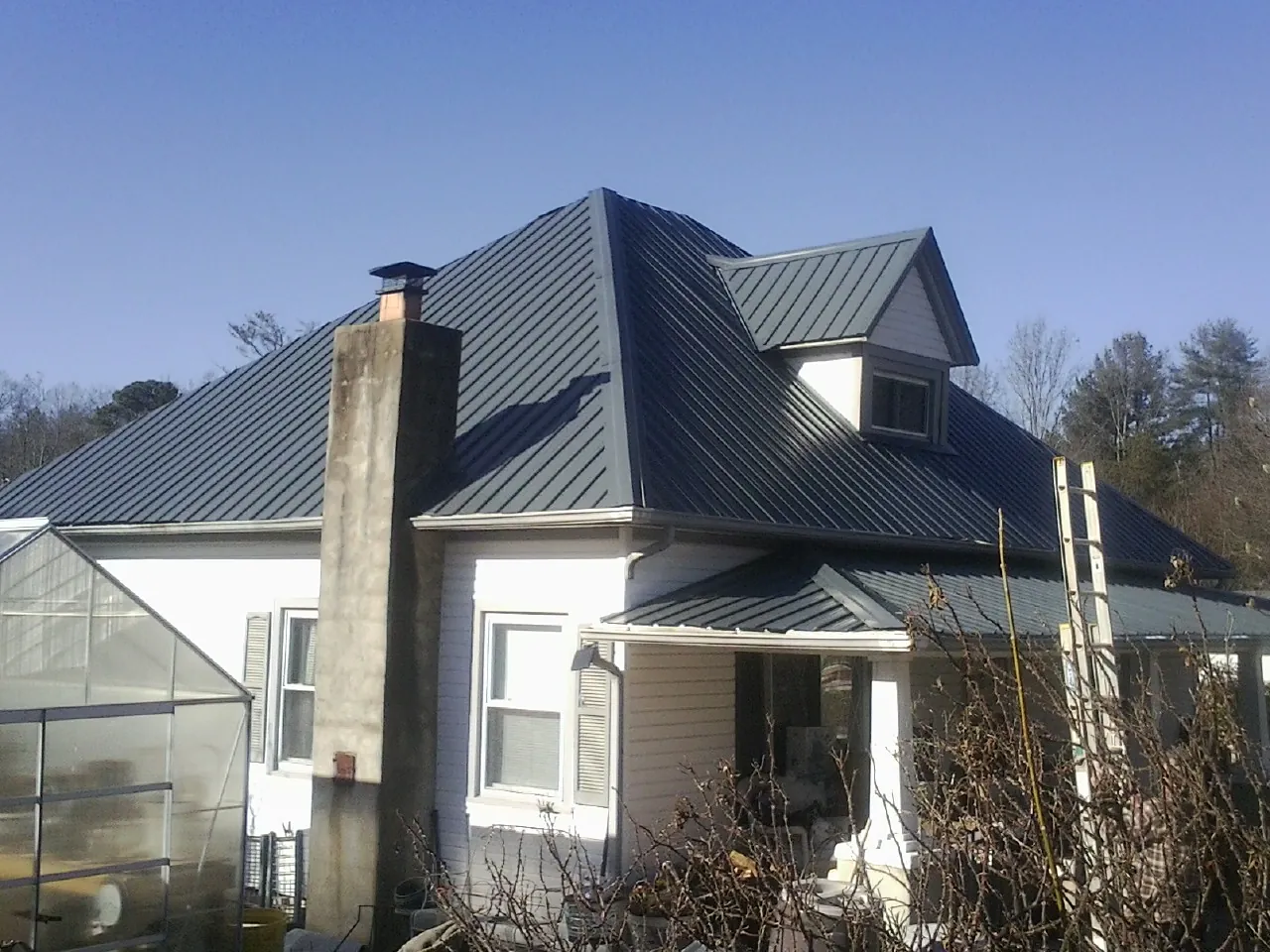 Dark blue standing seam metal roof on a white farmhouse with dormer — Slate & Tile Roof Repair by Roofing Brothers in Carmichael