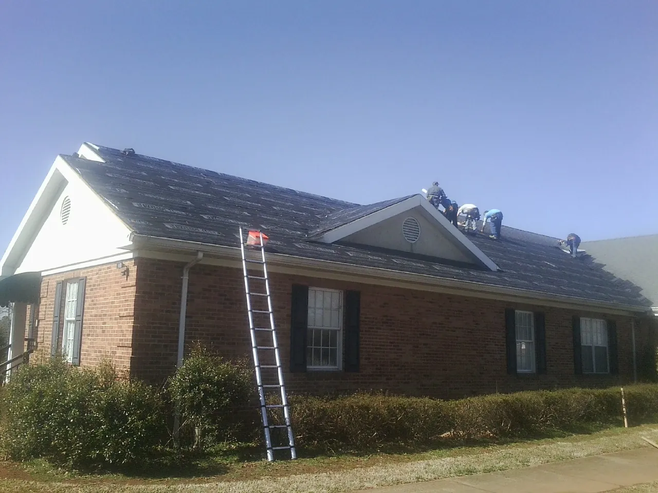 Crew tearing shingles off a brick ranch roof with a ladder set — Emergency Roof Repair work by our crew in Carmichael