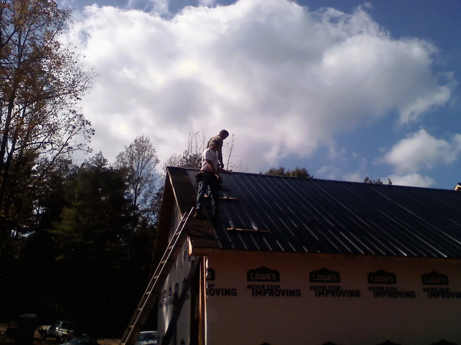 Roofer fastening dark metal panels high against a cloudy sky, from a Roof Inspection job in Carmichael