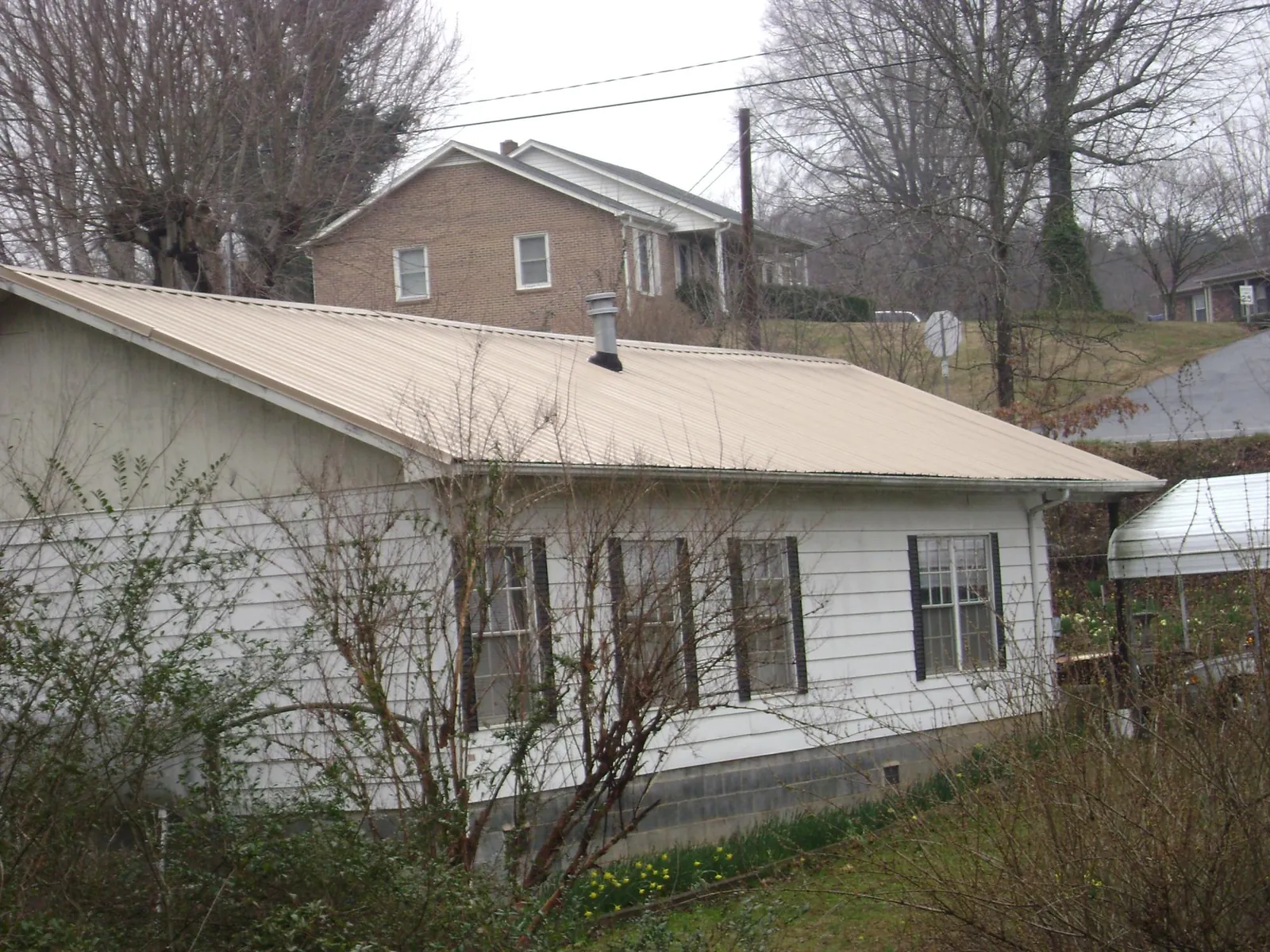 Tan metal roof on a white sided house set into a hillside — Commercial Roofing by Roofing Brothers in Carmichael